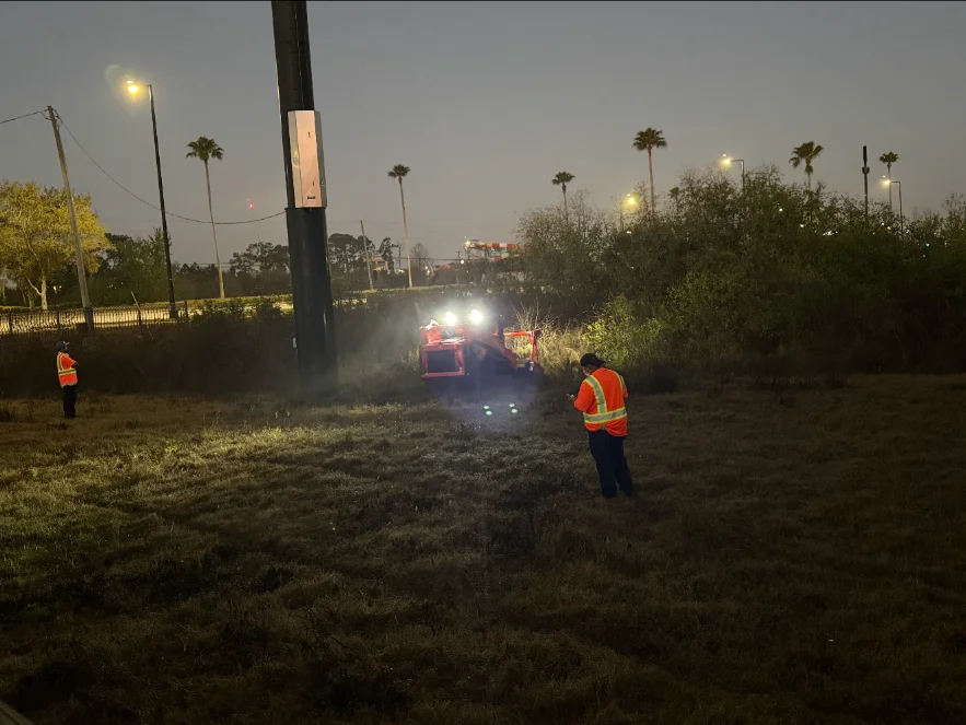 Crew running a forestry mulcher at dusk on a commercial clearing job
