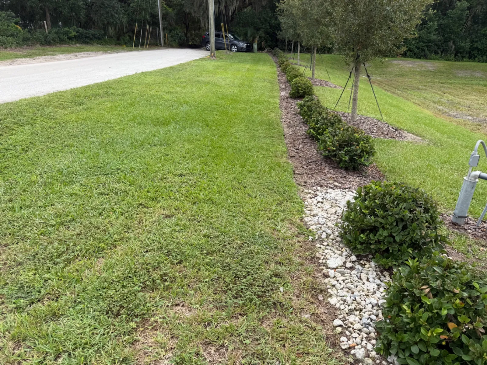 Mulched shrub bed with river rock beside a mowed lawn