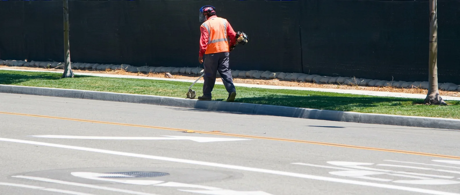 Crew member edging grass along a curb